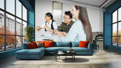 Side view portrait of smiling businesswoman in wheelchair enjoying meeting with colleagues in office Wall mural