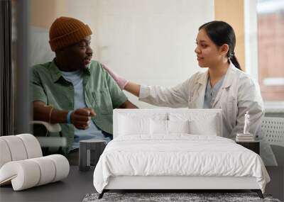 Side view portrait of smiling female doctor comforting patient receiving IV treatment in clinic Wall mural