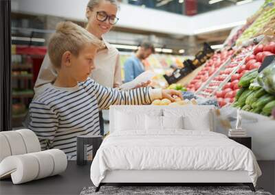 Side view portrait of teenage boy choosing fresh fruits at farmers market while grocery shopping with family, copy space Wall mural