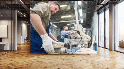 Side view portrait of two men wearing overalls working in factory shop operating modern machines, copy space Wall mural