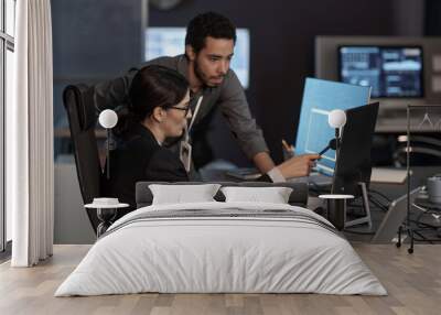 Side view portrait of two people pointing at computer screen while working in IT company Wall mural