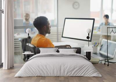 Side view portrait of young African-American man using computer in office, focus on blank white screen, copy space Wall mural