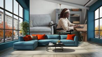 Side view portrait of young African-American woman using wheelchair while working from home in minimal grey interior, copy space Wall mural