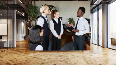 Side view portrait of young Black man as restaurant manager talking to servers wearing classic uniforms during morning instructions Wall mural