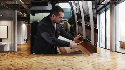 Side view portrait of young man building camper van and installing furniture in kitchen area Wall mural