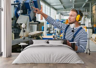 Side view portrait of young man pressing buttons on control panel while using metalworking machine in workshop Wall mural