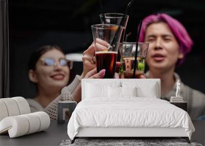 Three friends enjoying drinks at gathering while raising glasses in toast. Smiling and showing camaraderie, each holding different beverage in lively social setting Wall mural