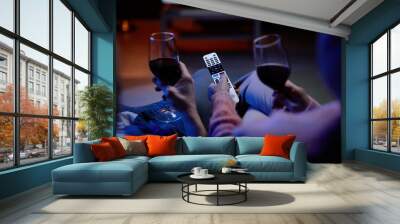 Top view closeup of unrecognizable senior couple watching TV together with hands holding remote control and wine glasses copy space Wall mural