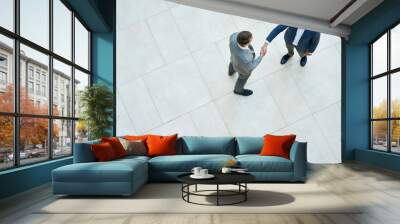 Top view of two business people shaking hands standing on tiled floor in hall of modern office building, copy space Wall mural