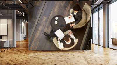 top view of two young elegant brokers sitting by table and discussing details of contract at working Wall mural