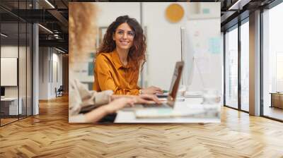 Two beautiful female colleagues interacting while working in office Wall mural