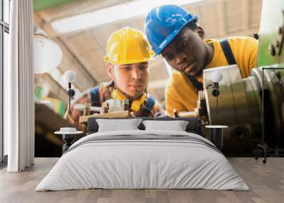 Two concentrated workers wearing protective helmets and rubber gloves using lathe in order to machine workpiece, interior of plant production department on background Wall mural