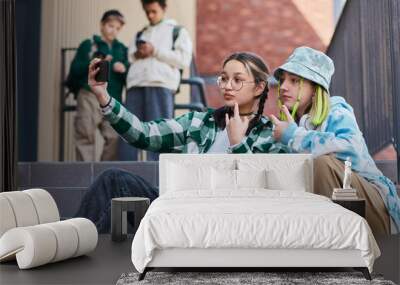 Two teenage girls sitting on stairs of school building and making selfie portrait on smartphone Wall mural