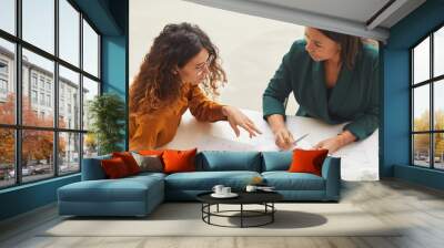 two young businesswomen working on new business plan sitting together at office desk, high angle hor Wall mural