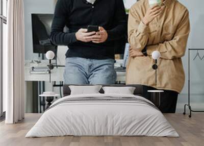 Two young intercultural businessmen in casual clothes standing by desk with computer monitor and discussing their plans for the night Wall mural