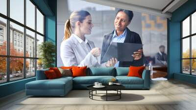 Two young intercultural businesswomen discussing online data for report in conference hall Wall mural