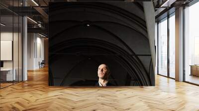 Vertical image of mature man with Bible standing in old church with beautiful architecture and praying Wall mural