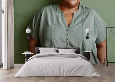 Vertical portrait of black senior woman wearing glasses and smiling at camera while standing against green background Wall mural