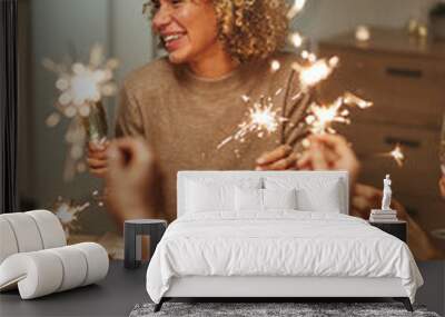 Vertical portrait of carefree mixed-race woman holding sparklers while enjoying dinner party and celebration with friends and family Wall mural