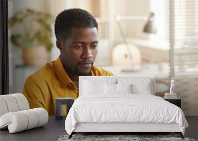 Vertical portrait of contemporary African-American man using laptop while sitting at white desk in office, copy space above Wall mural