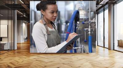 Vertical portrait of young African-American woman holding clipboard while inspecting production quality at industrial food factory, copy space Wall mural