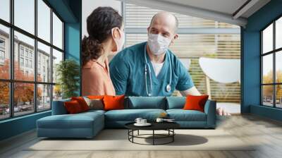 Vertical portrait of young woman wearing mask while talking to veterinarian in waiting room at vet clinic with white dog Wall mural