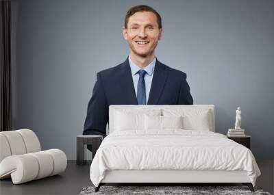 Waist up portrait of adult Caucasian man wearing business suit and smiling at camera while standing against grey background in studio, copy space Wall mural