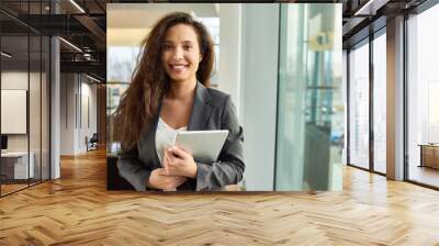 Waist-up portrait of attractive young businesswoman in formalwear posing for photography with charming smile while holding digital tablet in hands, interior of spacious office lobby on background Wall mural