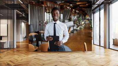 Waist up portrait of Black young man as restaurant manager smiling at camera standing in dining room, copy space Wall mural