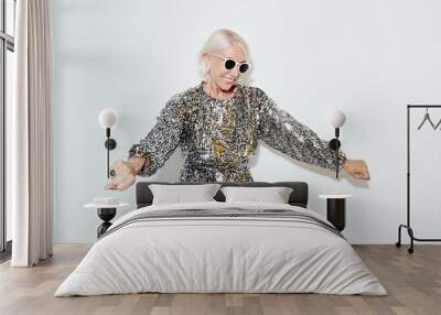 Waist up portrait of cool mature woman wearing glamour dress while dancing at party against white wall, shot with flash Wall mural