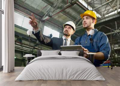 Waist up portrait of handsome businessman pointing up while discussing something with factory worker holding digital tablet, copy space Wall mural