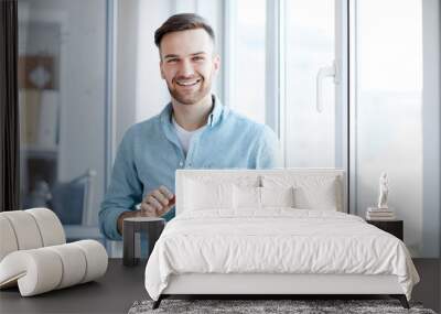 Waist up portrait of handsome young man holding digital tablet and smiling happily at camera standing by window, copy space Wall mural