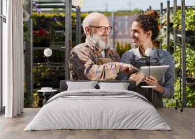 Waist up portrait of smiling senior farmer using digital tablet while instructing young female worker in plantation lit by sunlight, copy space Wall mural