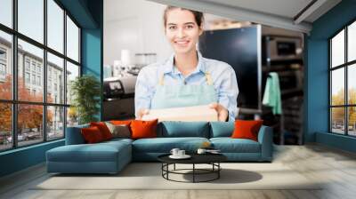 Waist up  portrait of smiling young  woman wearing apron holding box with takeaway food and looking at camera, copy space Wall mural