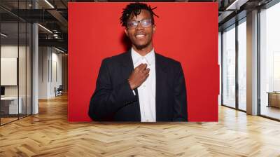 Waist up portrait of trendy African-American man smiling cheerfully while posing against red background, shot with flash Wall mural