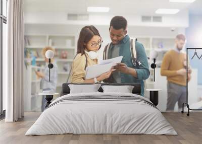 Waist up portrait of two international students reading book while standing in college library, copy space Wall mural