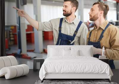 Waist up portrait of two modern bearded mechanics walking across workshop and pointing away  while working in car service and repair center, copy space Wall mural