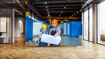 Waist up portrait of two modern factory workers wearing hardhats holding blueprints  while discussing production in workshop, copy space Wall mural