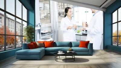 Waist up portrait of two modern young scientists wearing lab coats  chatting while taking break from working in medical laboratory Wall mural