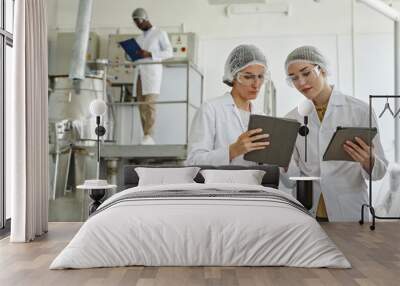 Waist up portrait of two young women wearing lab coats and using digital tablet in workshop of pharmaceutical factory, copy space Wall mural