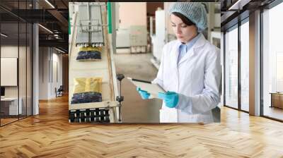 Waist up portrait of young woman controlling production  process at modern food factory and using digital tablet while standing by packaging line, copy space Wall mural