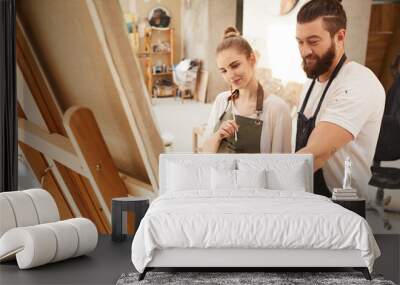 Warm toned portrait of creative couple painting picture together and smiling happily while standing by easel in sunlit art studio, copy space Wall mural