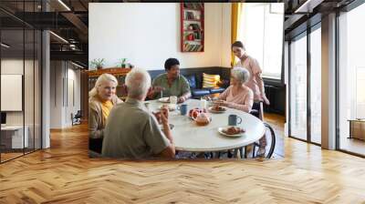 Warm-toned portrait of diverse group of senior people enjoying breakfast in cozy nursing home, copy space Wall mural