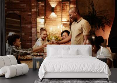 Warm toned portrait of happy African-American family clinking glasses and toasting while enjoying dinner together at evening Wall mural