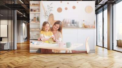 Warm-toned portrait of happy mother hugging little daughter while drawing pictures at wooden kitchen table, copy space Wall mural