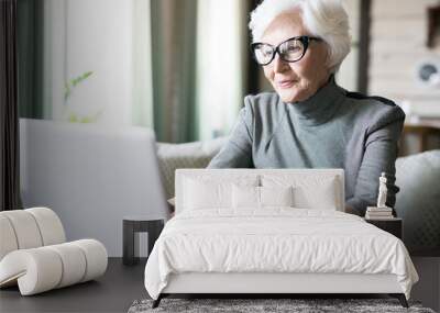 white haired senior woman wearing eyeglasses sitting at cafe and using her laptop Wall mural