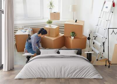 Wide angle background of young Asian woman packing cardboard boxes in empty white room, moving, relocation and house decor concept, copy space Wall mural