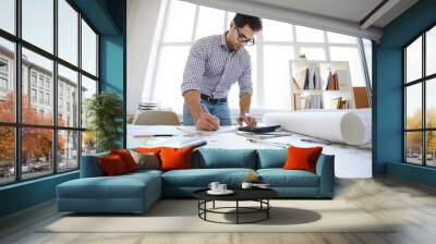 Wide angle portrait of engineer drawing plans and making measurements at workplace, copy space Wall mural