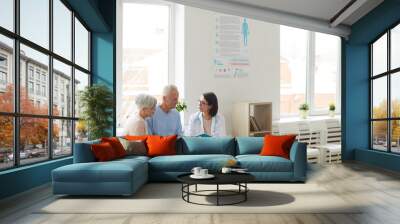 Wide angle portrait of young female doctor talking to senior couple while sitting in reception area of modern clinic, copy space Wall mural