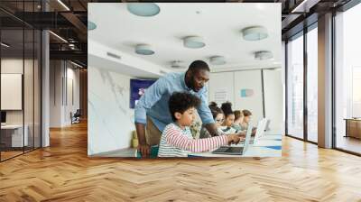 Wide angle side view portrait of young boy using computer in IT class with male teacher helping him, copy space Wall mural